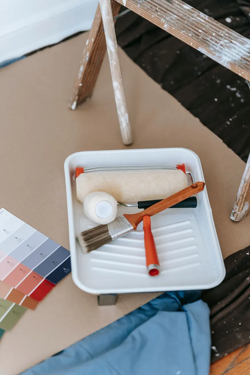 A paint tray with a roller and brush beside a fan of colour swatches